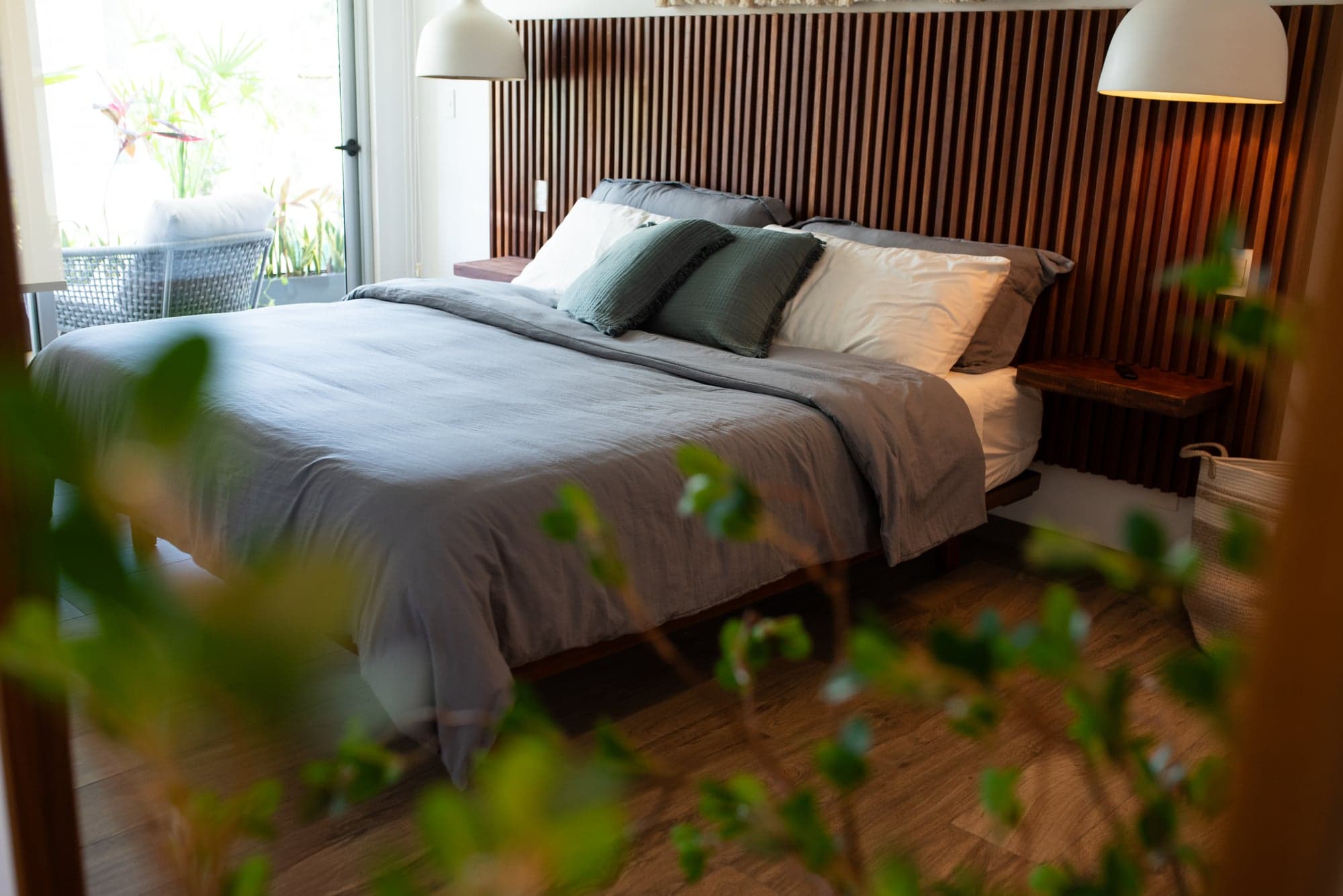 Primary suite with wood slat headboard, grey linens, and green accent pillows at The Leaf Playacar